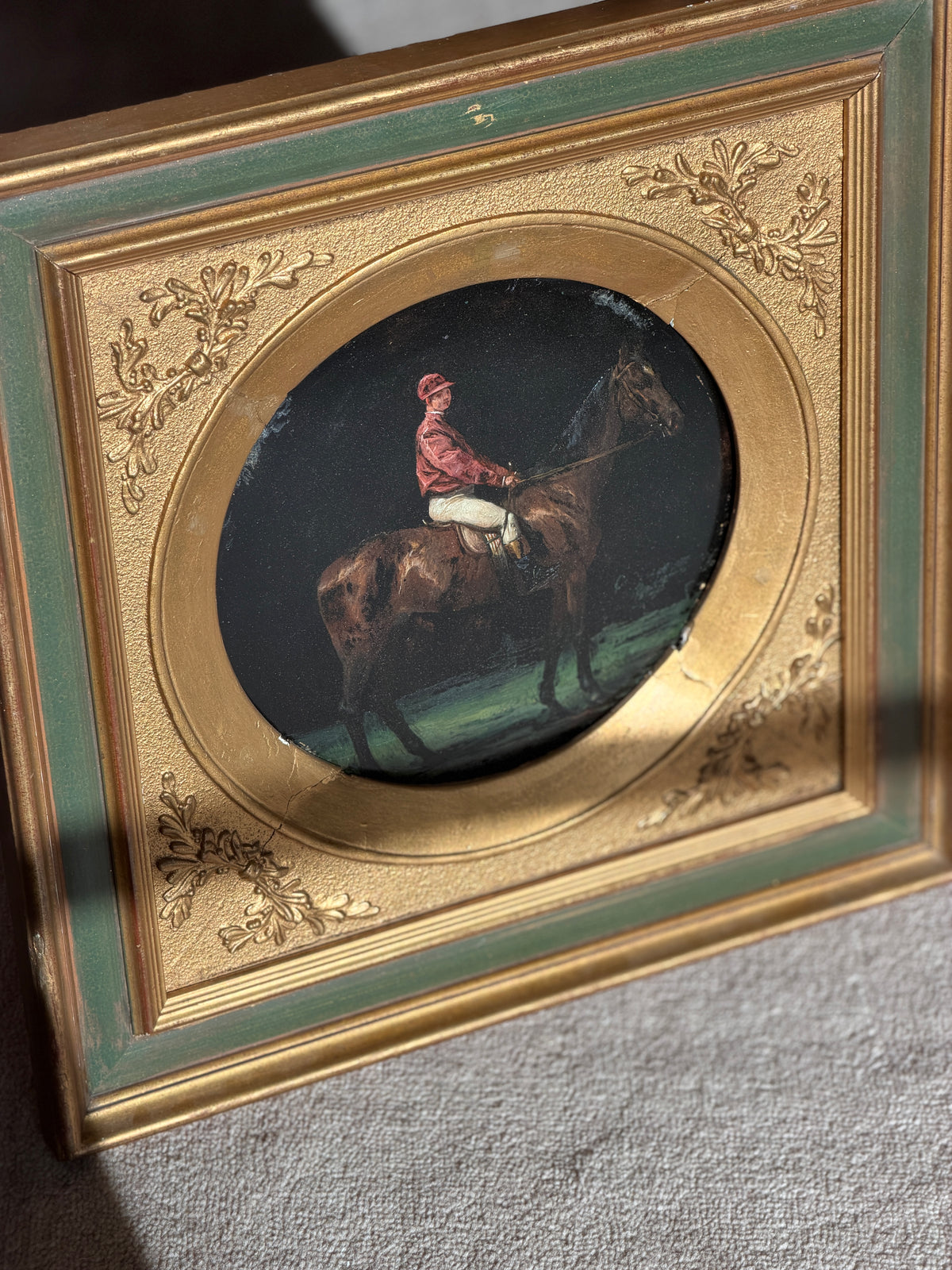 Close angled detail of the painted bay horse and red jacketed rider, with visible age cracks and losses to the gilt round mat