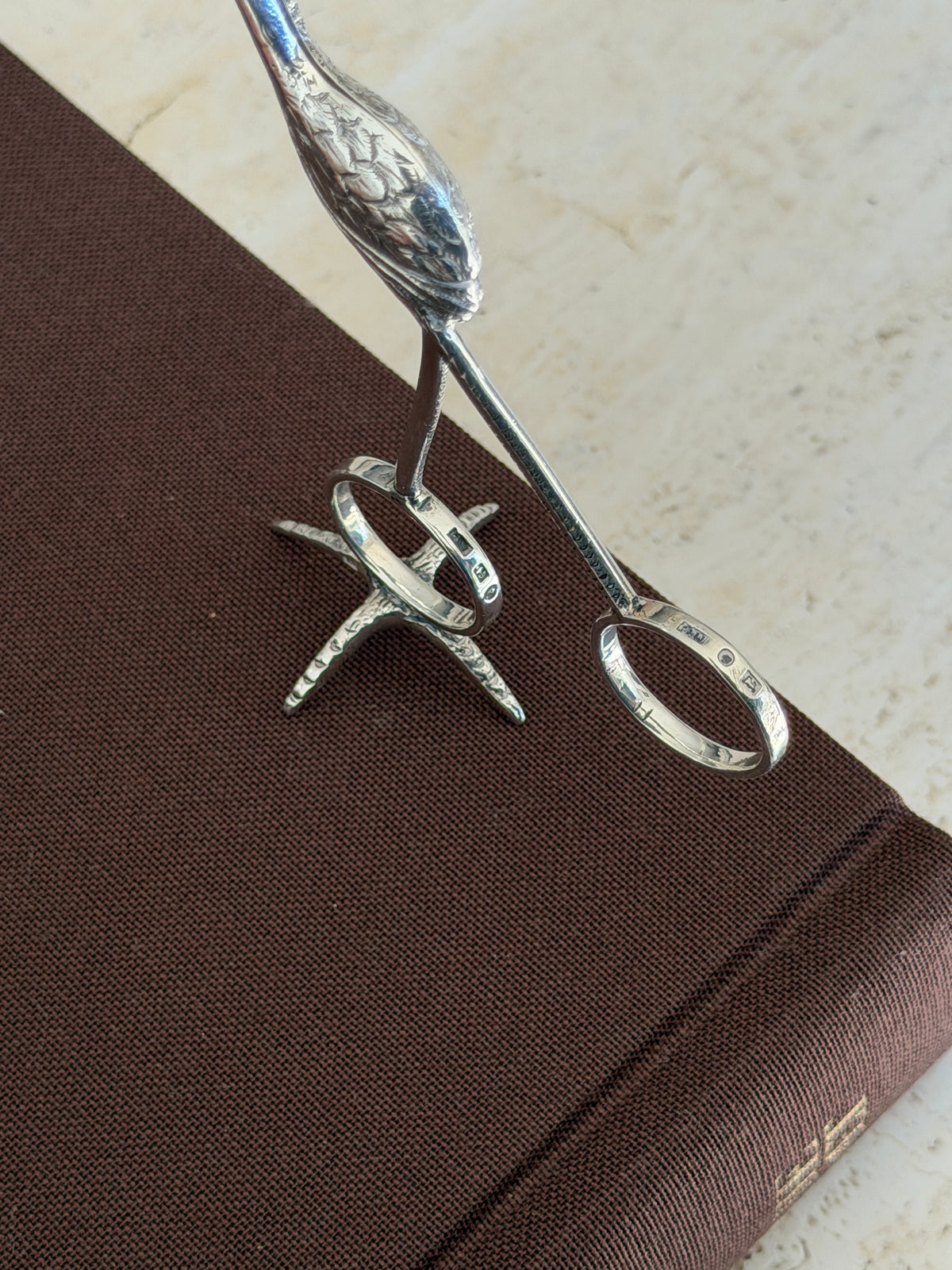 Close view of the flamingo tongs ring handles, both stamped with Birmingham hallmarks, above the textured foot stand