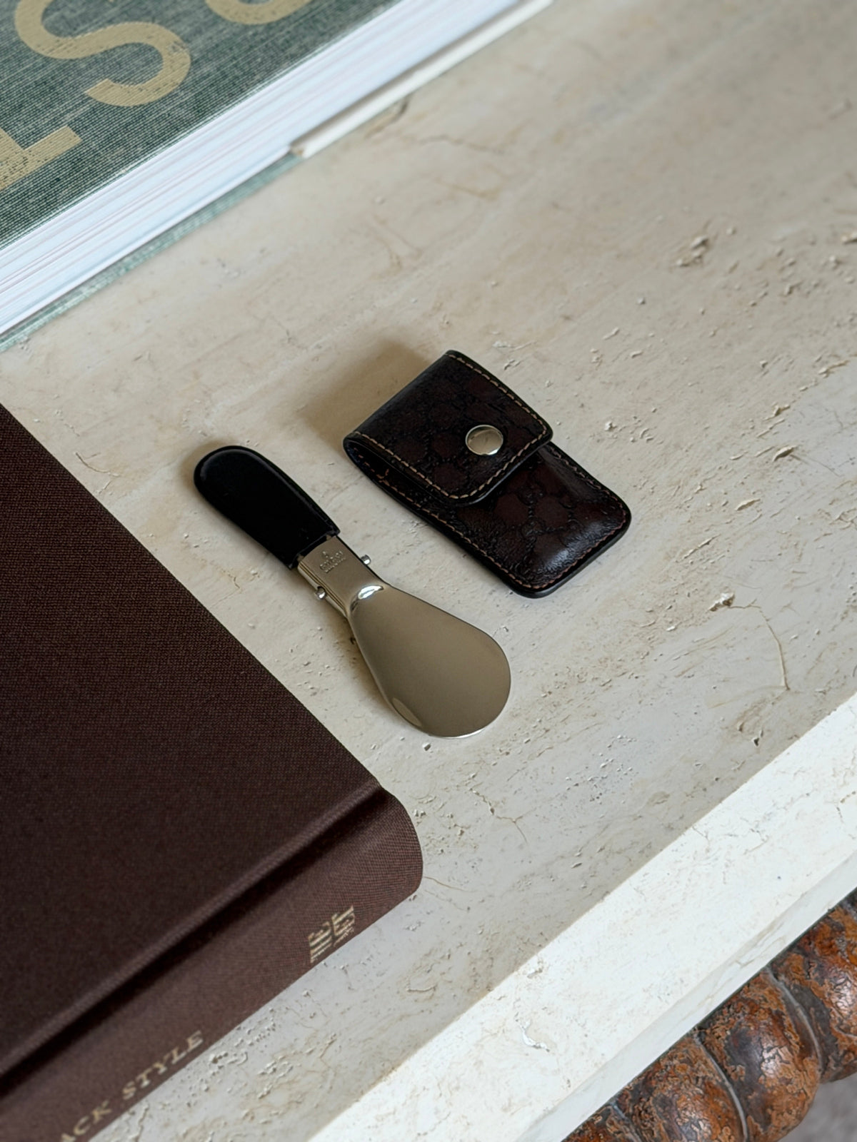 Angled overhead view of the folded Gucci shoehorn and case styled near stacked books