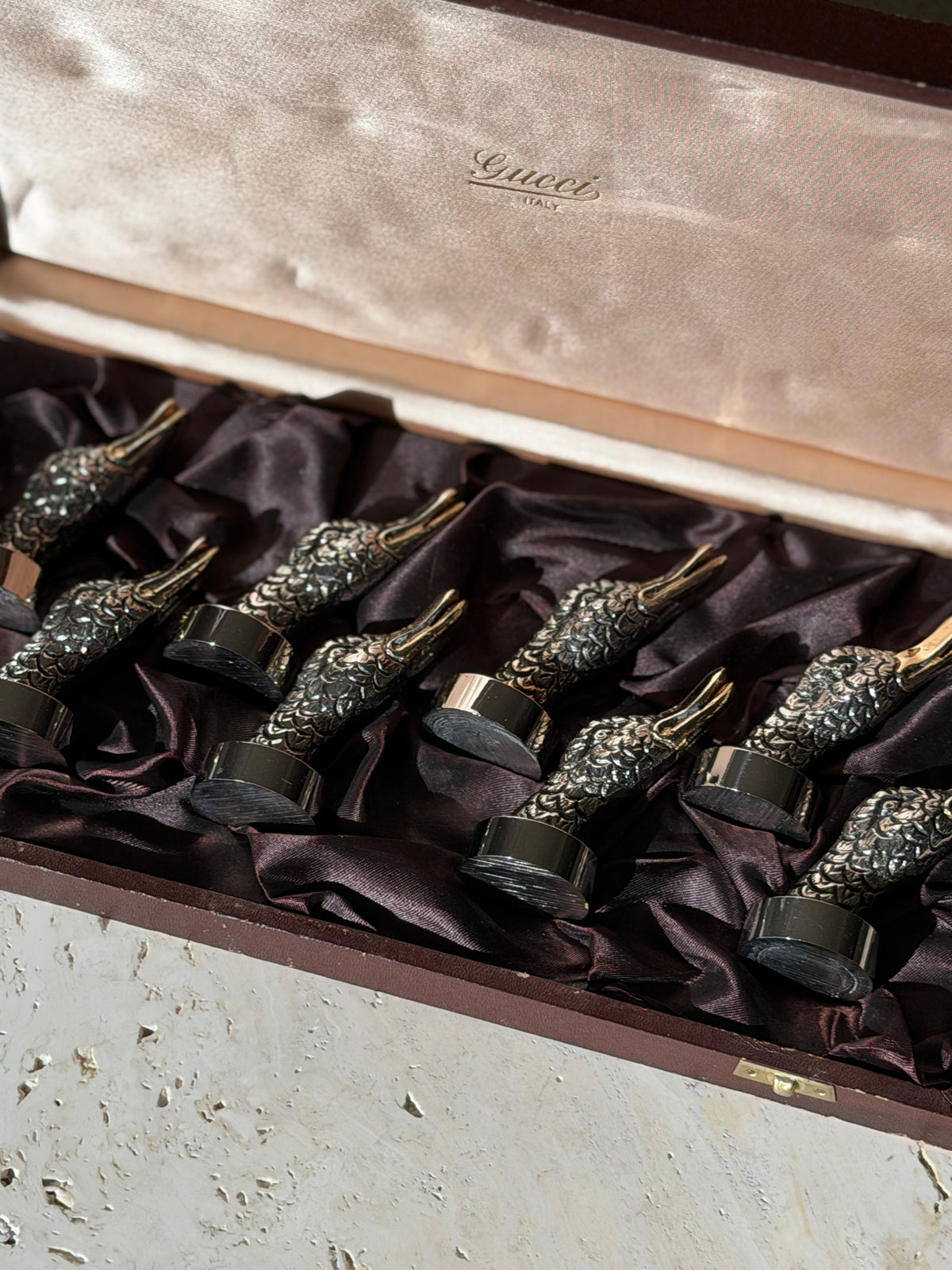 Low angle view of the duck head place card holders in the box, sunlight catching the feather texture below the Gucci Italy lid lining