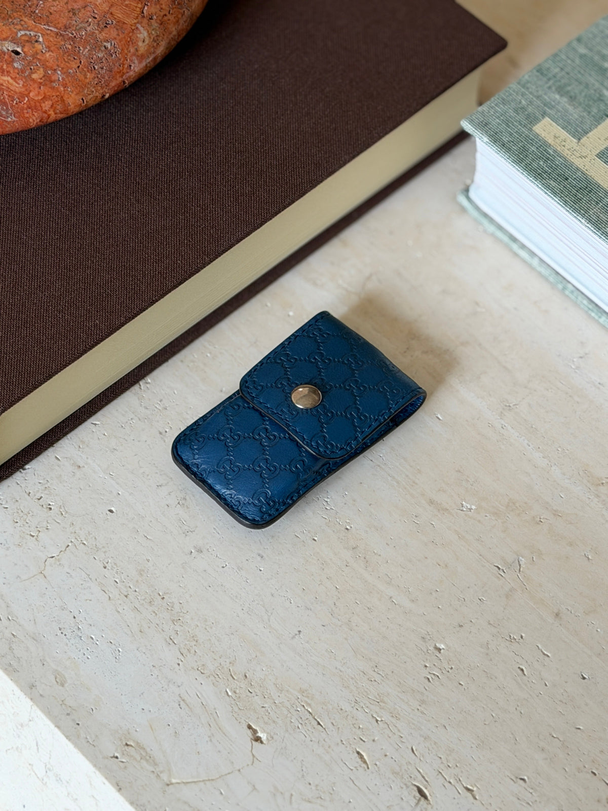 Angled view of the blue leather Gucci monogram case on a painted table surface