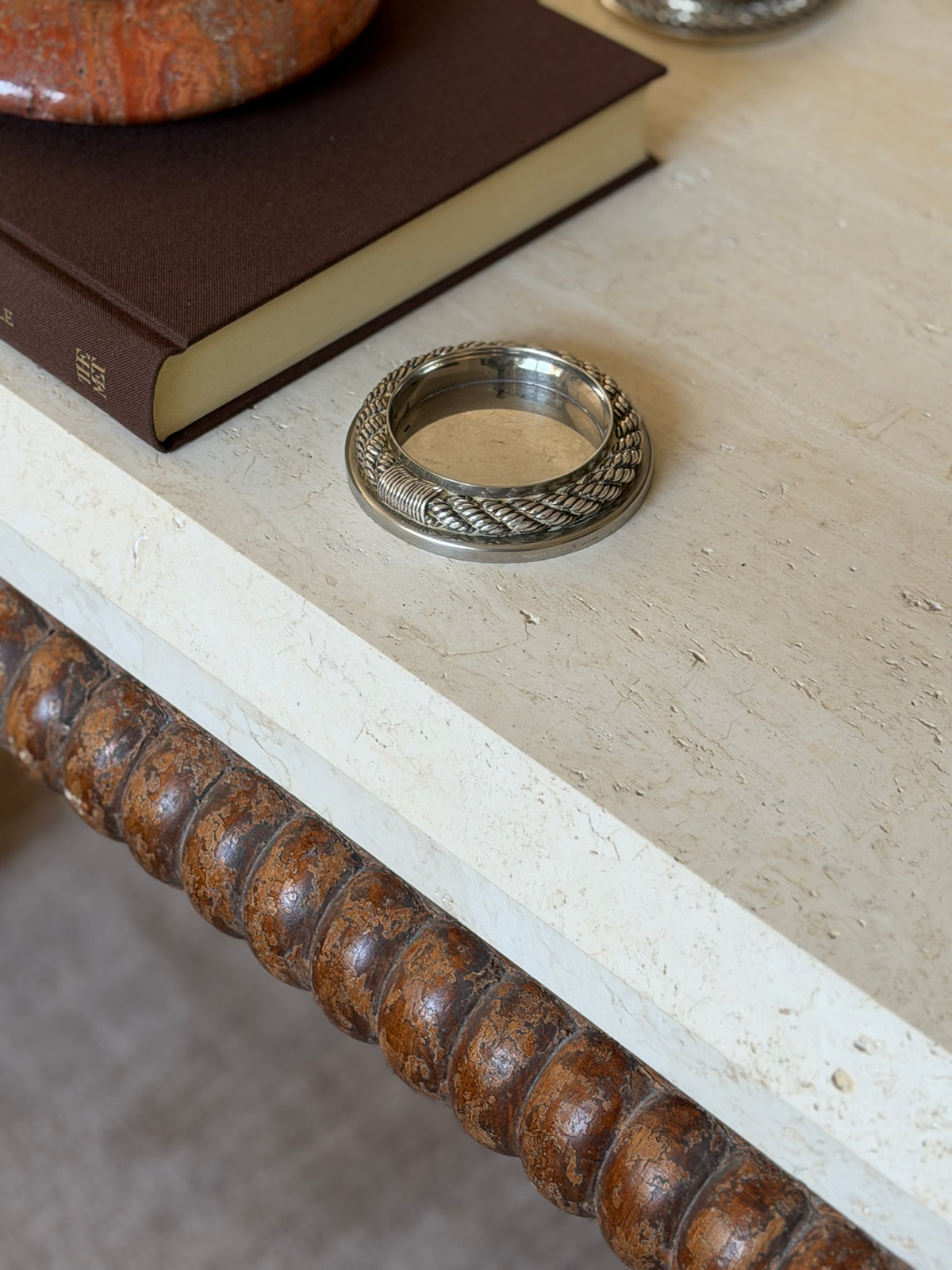 Low angle view of the Hermes rope coaster near the edge of a travertine table, highlighting its raised inner wall above a bobbin-turned wood table base