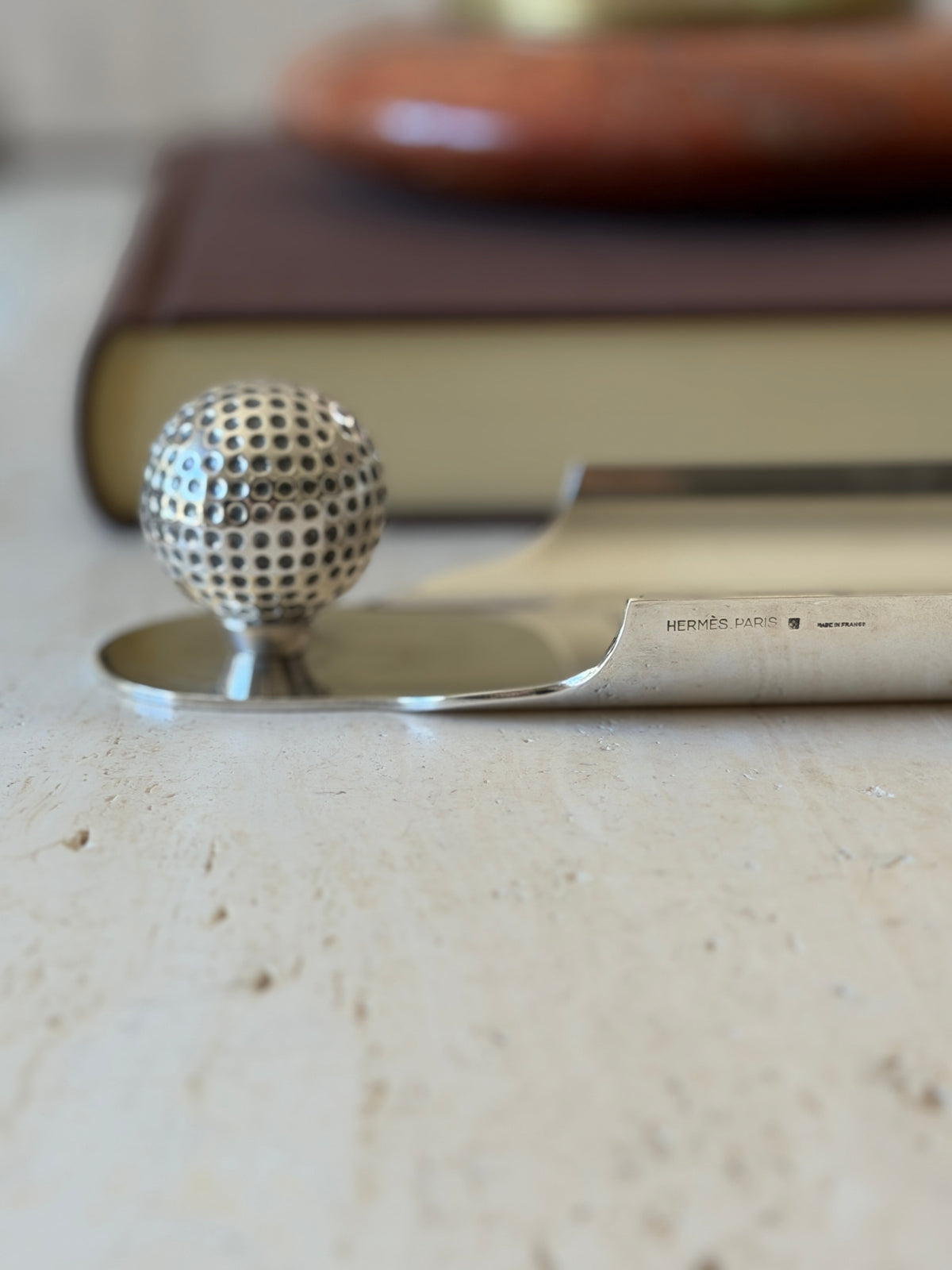 Low eye level view of the Hermes tray edge stamped HERMES PARIS and Made in France, the golf ball rising at the end