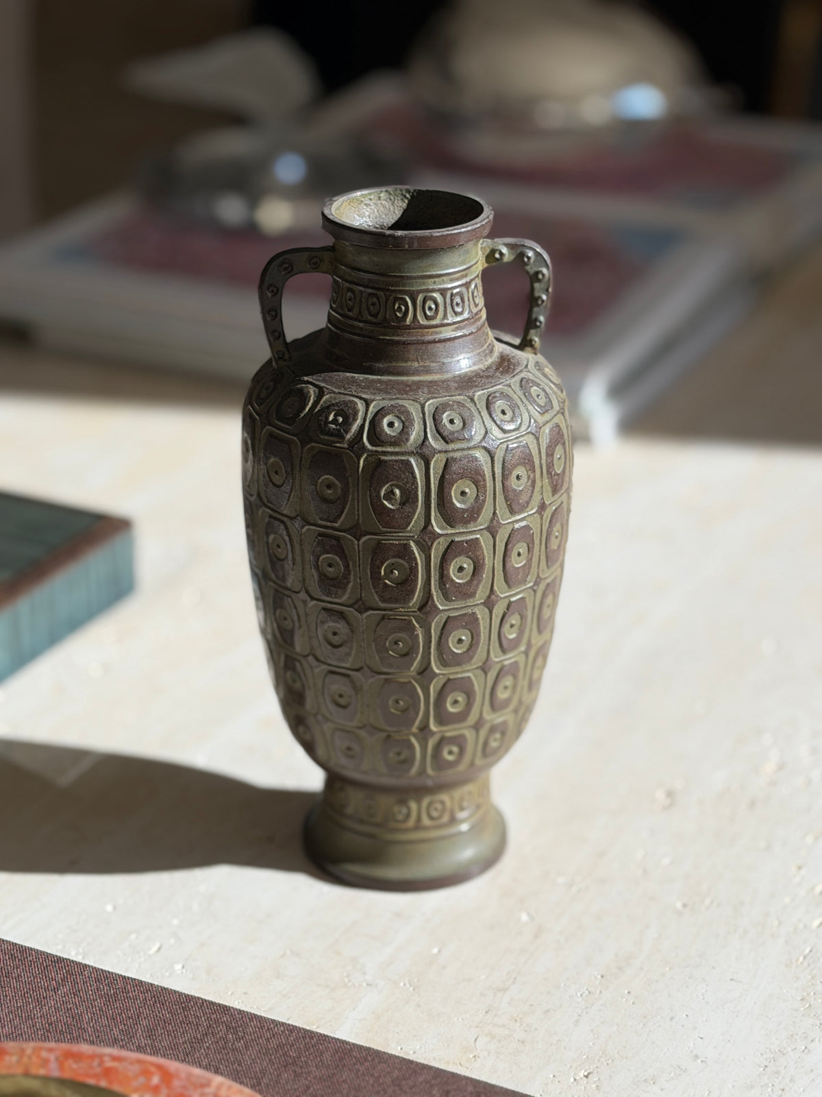 Close view of the geometric relief on the bronze vase, the green and russet patina highlighting each raised square and ring
