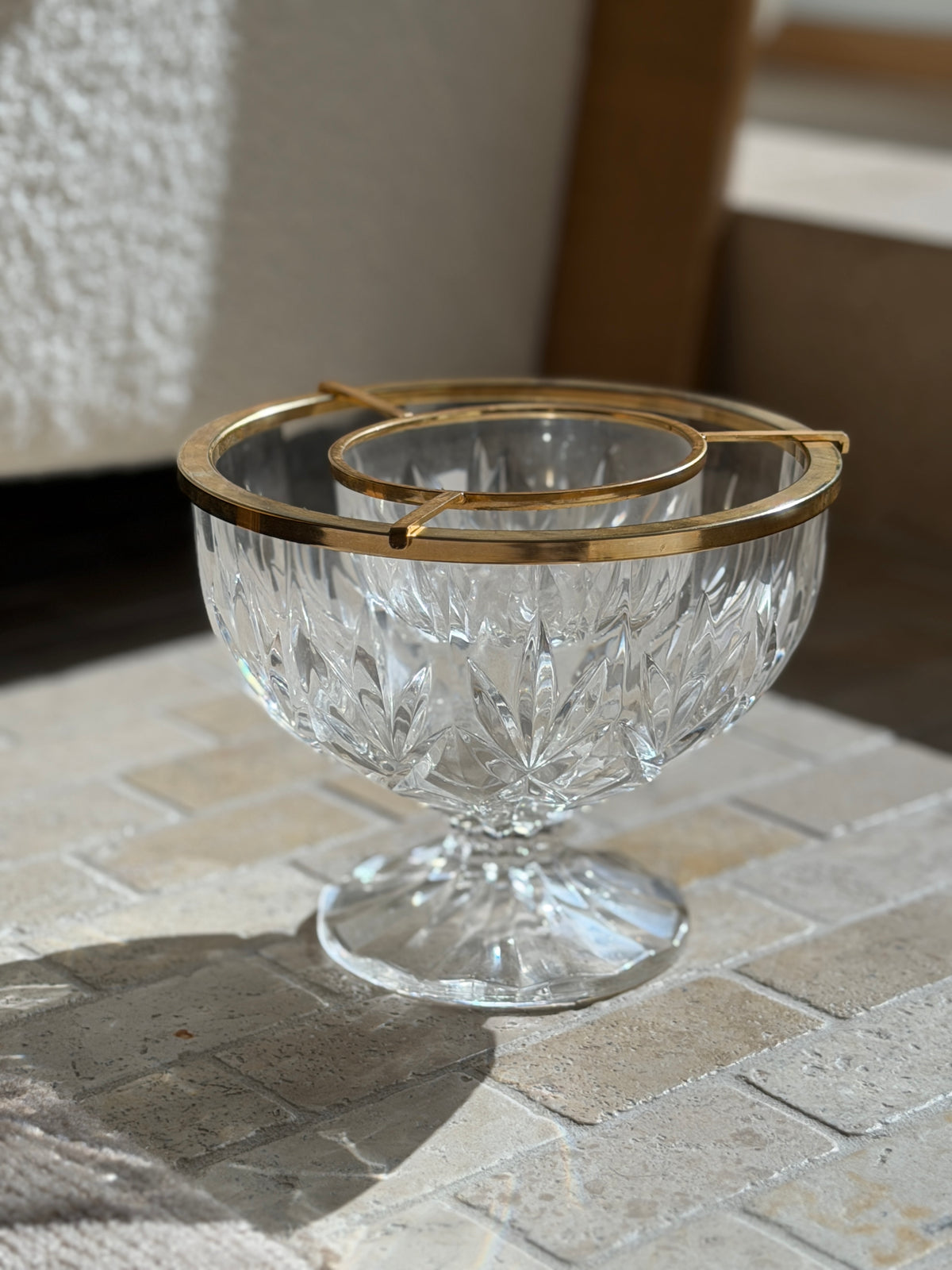 Close three quarter view of the caviar dish against a boucle chair, the polished gilt frame resting on the crystal rim