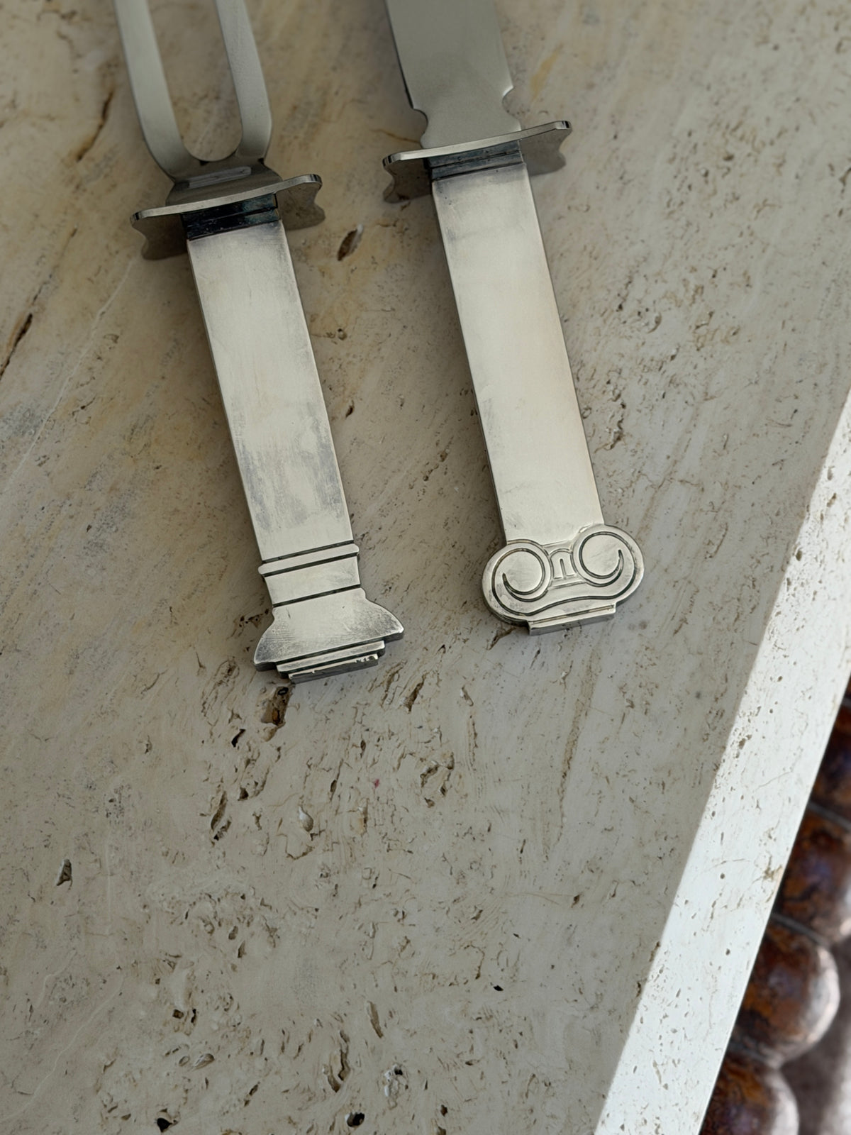 Close view of the carving set handles showing the engraved Ionic volute pommel on the knife and the banded, stepped column base on the fork