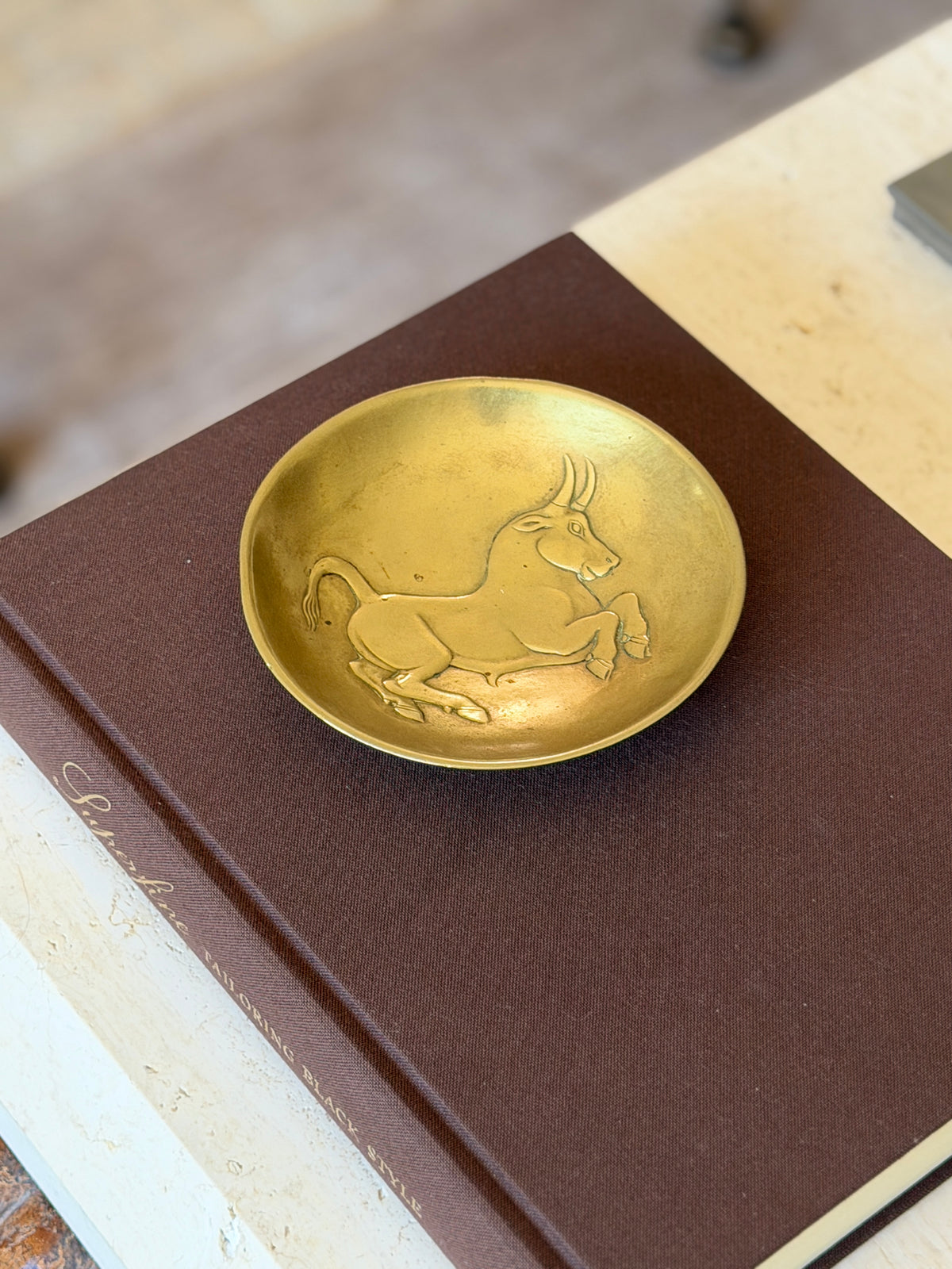 Gilded bronze bull bowl resting on the Superfine Tailoring Black Style book, the relief catching warm light