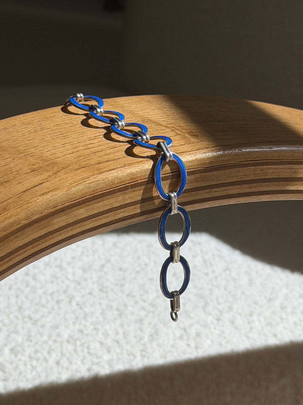 Blue enamel and sterling silver bracelet draped over a bentwood oak chair arm, hanging free to show the ring end and full run of oval links