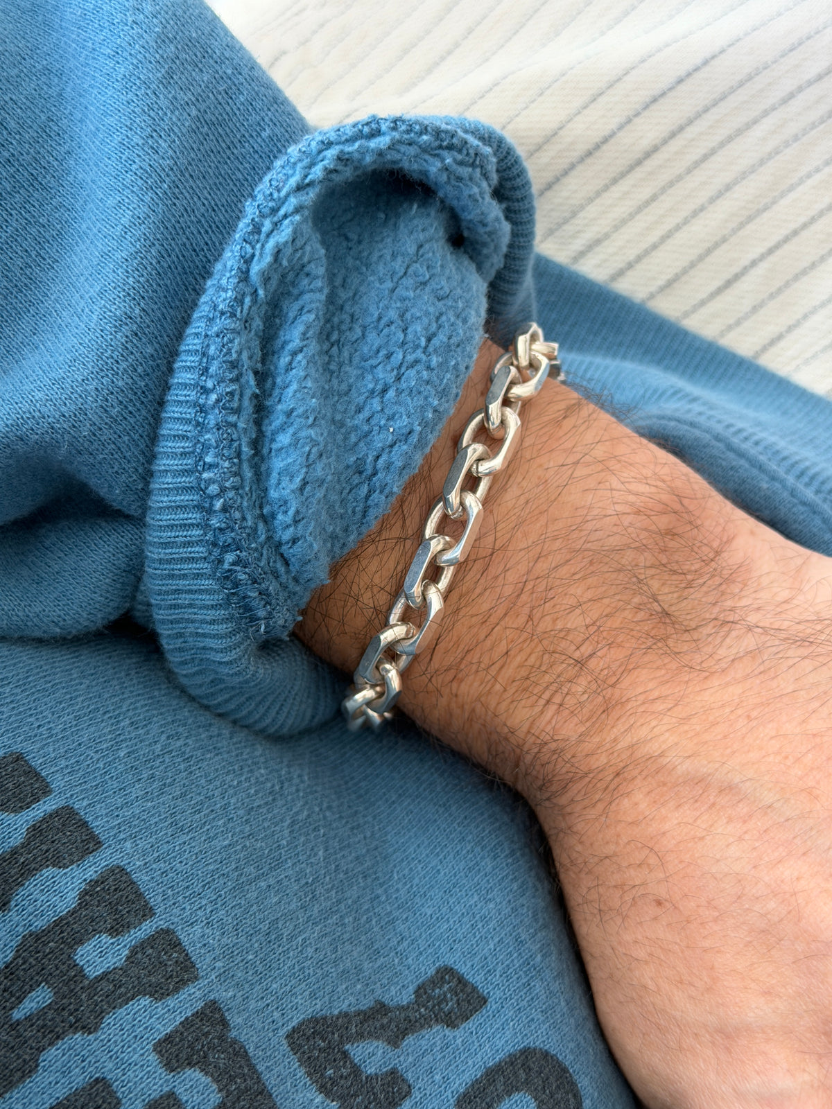 Bracelet worn on the wrist against a ribbed cream top and printed sweatshirt sleeve