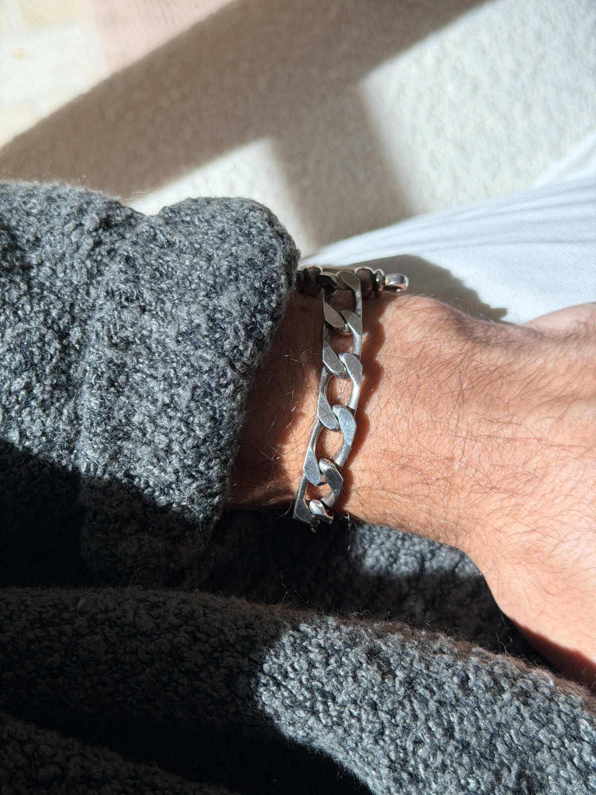 Wrist view of the heavy beveled curb chain section of the bracelet, the shackle pin just visible at the cuff