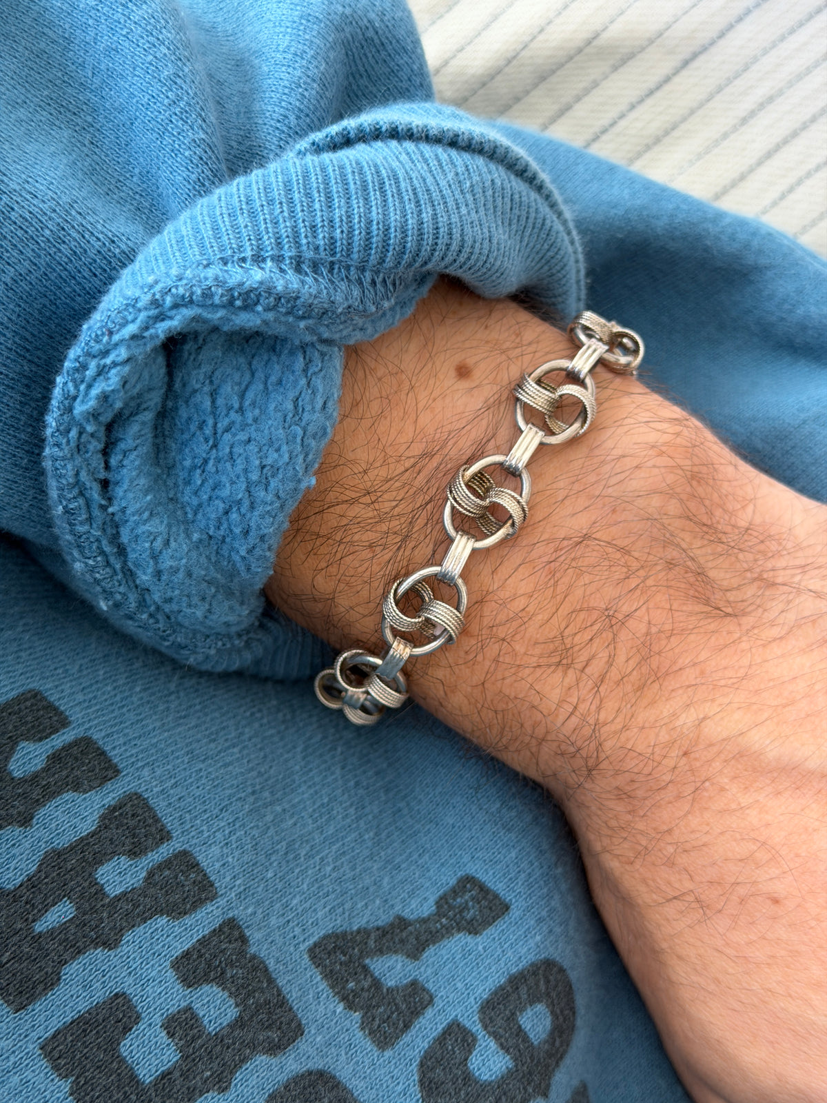 Bracelet worn on the wrist against a printed sweatshirt and cream carpet