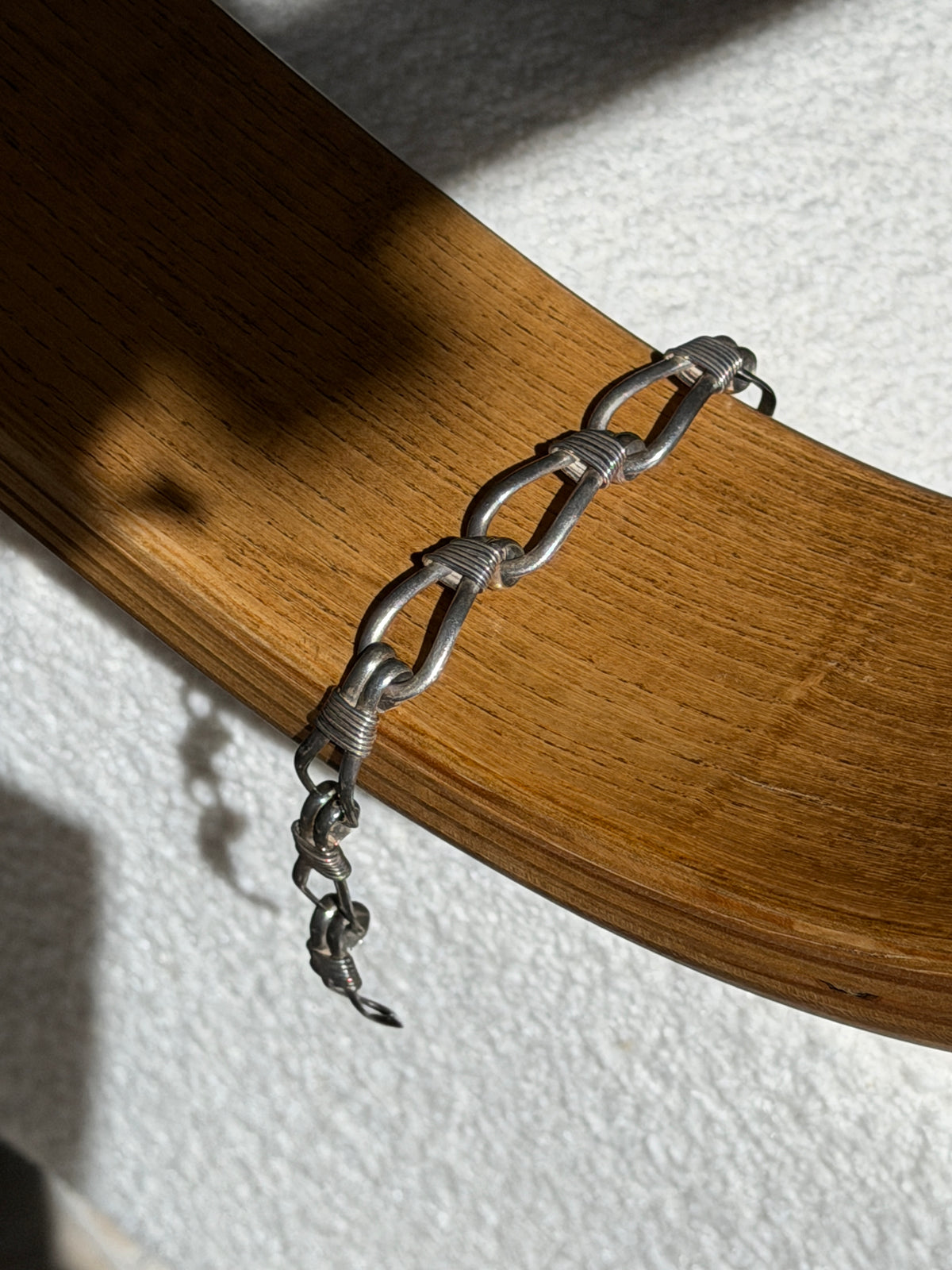 Sterling nautical rope bracelet draped over a bentwood oak chair arm, the lashed loops and hook clasp end hanging free