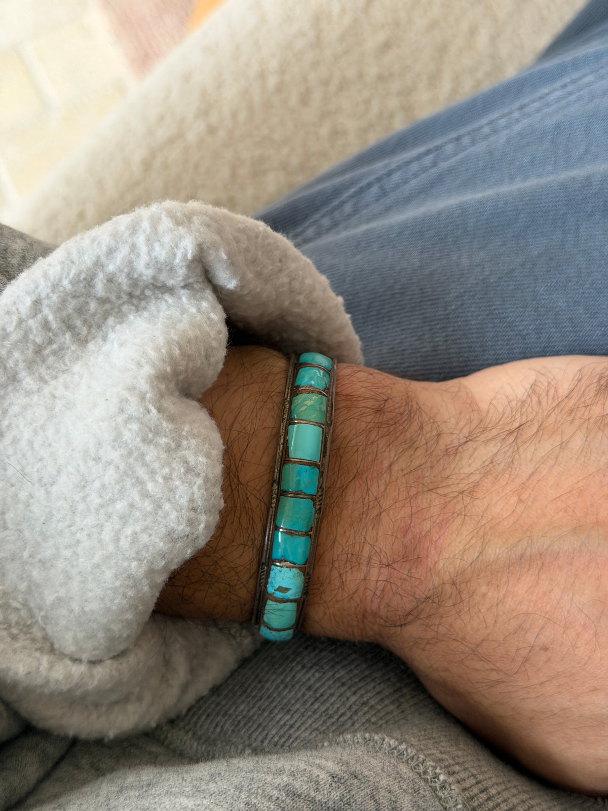 Cuff worn on the wrist over a grey sweatshirt cuff, with blue jeans in the background