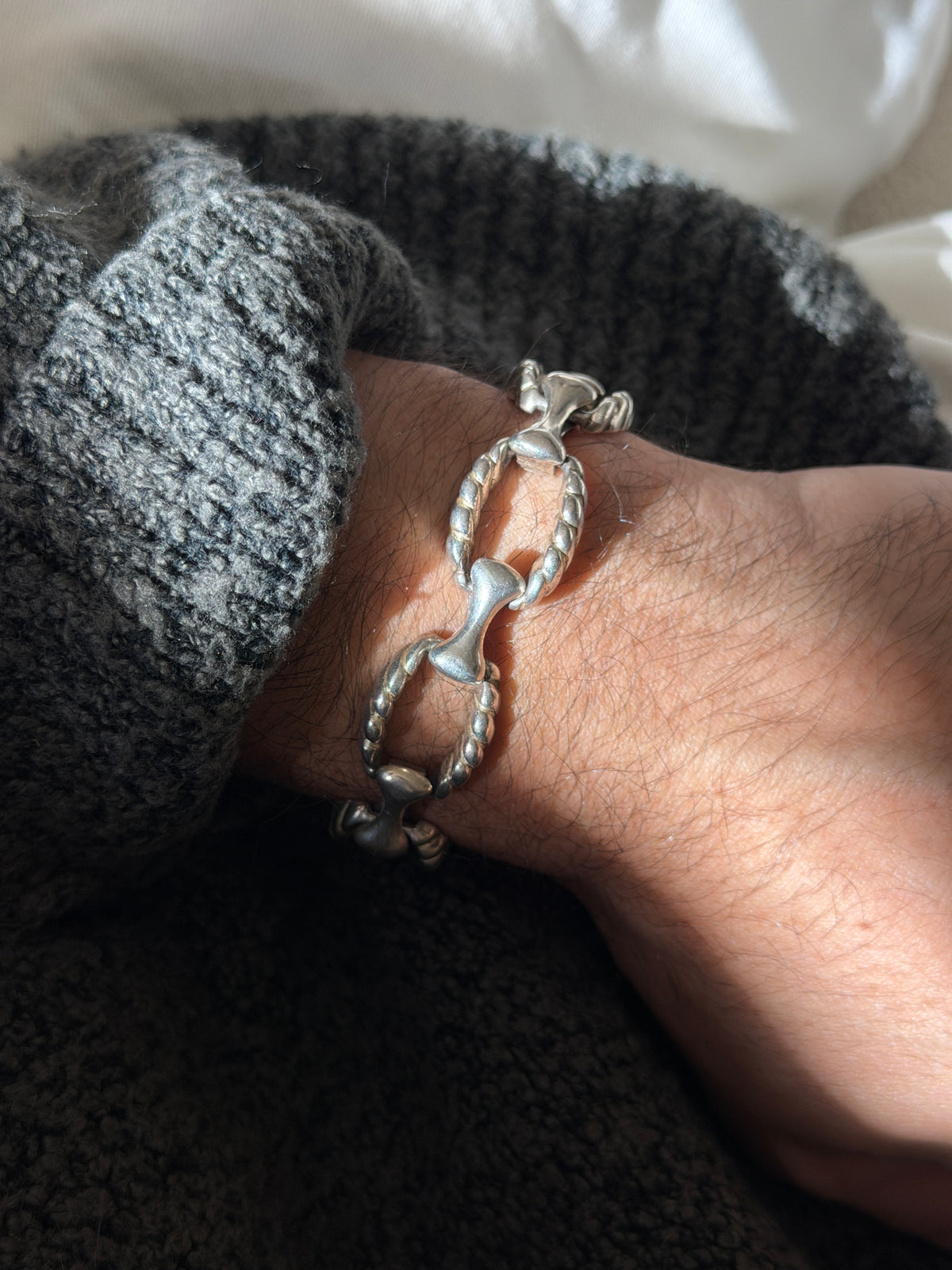 Vintage sterling silver bracelet of twisted rope oval links joined by sculpted bone shaped connectors, worn on the wrist in sunlight
