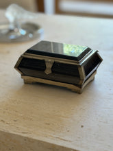 Front view of the stone and silver mounted box on travertine, window light reflecting across the polished lid and banded dark stone sides