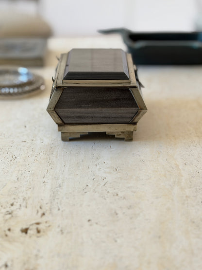End view of the stone box showing the faceted hexagonal profile, the banded stone grain, and cutout stepped feet on the base