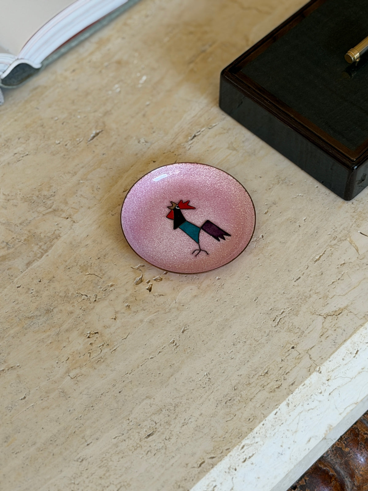 Overhead view of the dish on the travertine table beside a black lacquered box with a pen resting inside it