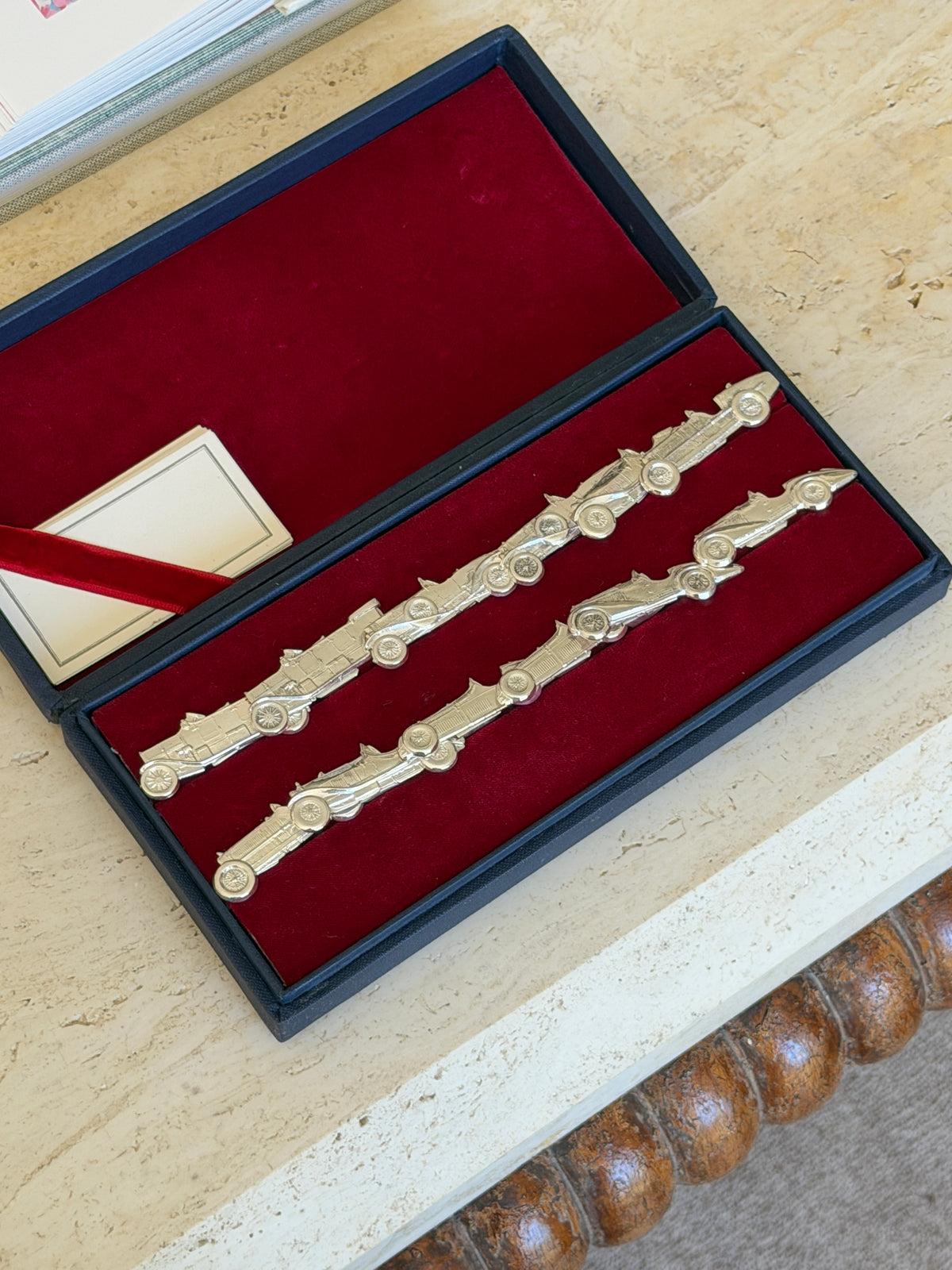 Open presentation box showing two rows of silver car-shaped place card holders on red velvet, with a ribbon-tied card in the corner