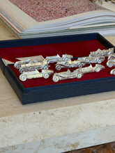 Close angled view of several vintage car-shaped place card holders arranged in the velvet-lined box
