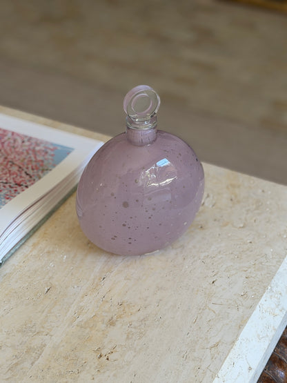 Alfredo Barbini Murano glass decanter in opaque lilac with white speckles and a clear disc stopper, on travertine beside an open art book