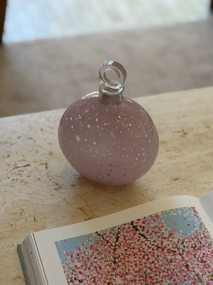 Barbini blown glass decanter on a travertine table in soft light, the lilac body scattered with white spots and fine bubbles