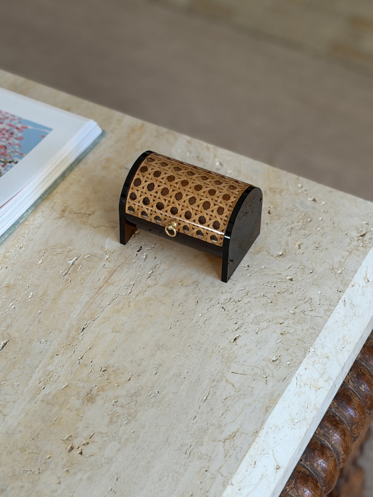 Front view of the 1970s Italian box showing the open hexagonal cane weave under clear Lucite and the small brass ring pull, with an art book nearby