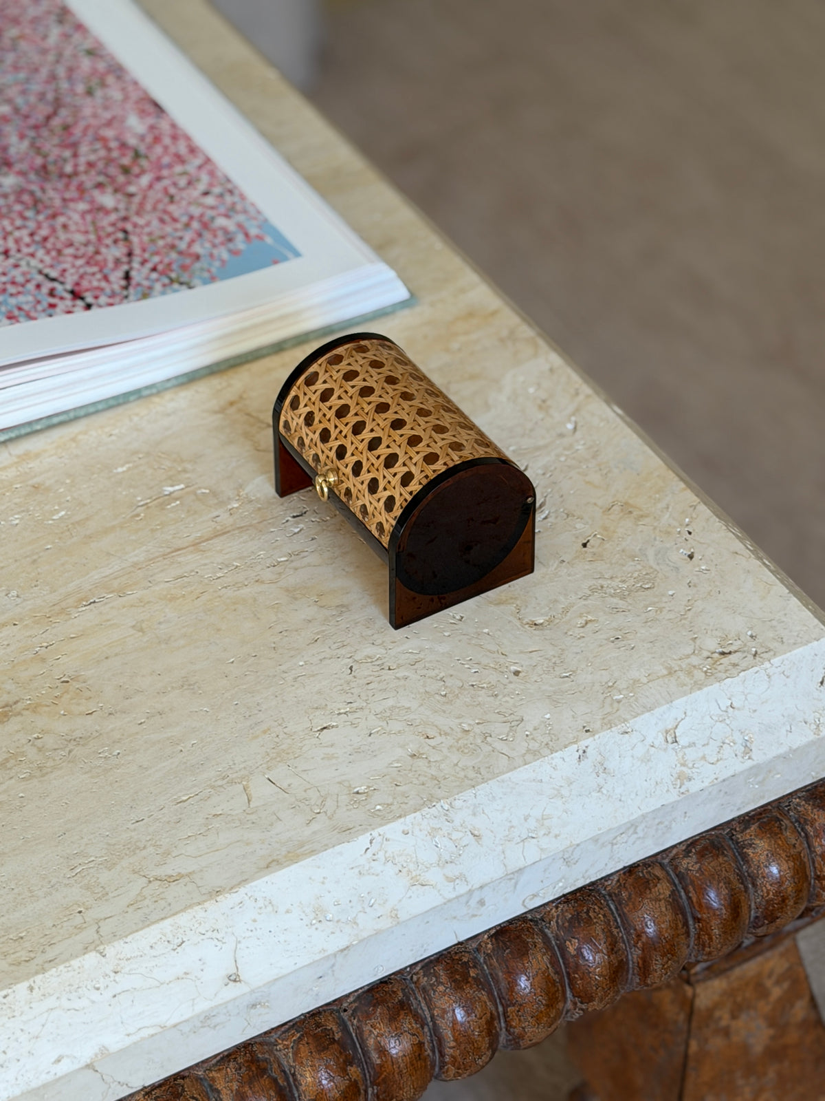 Amber Lucite, cane, and brass box resting near the corner of a travertine table with a bobbin-turned wood base below