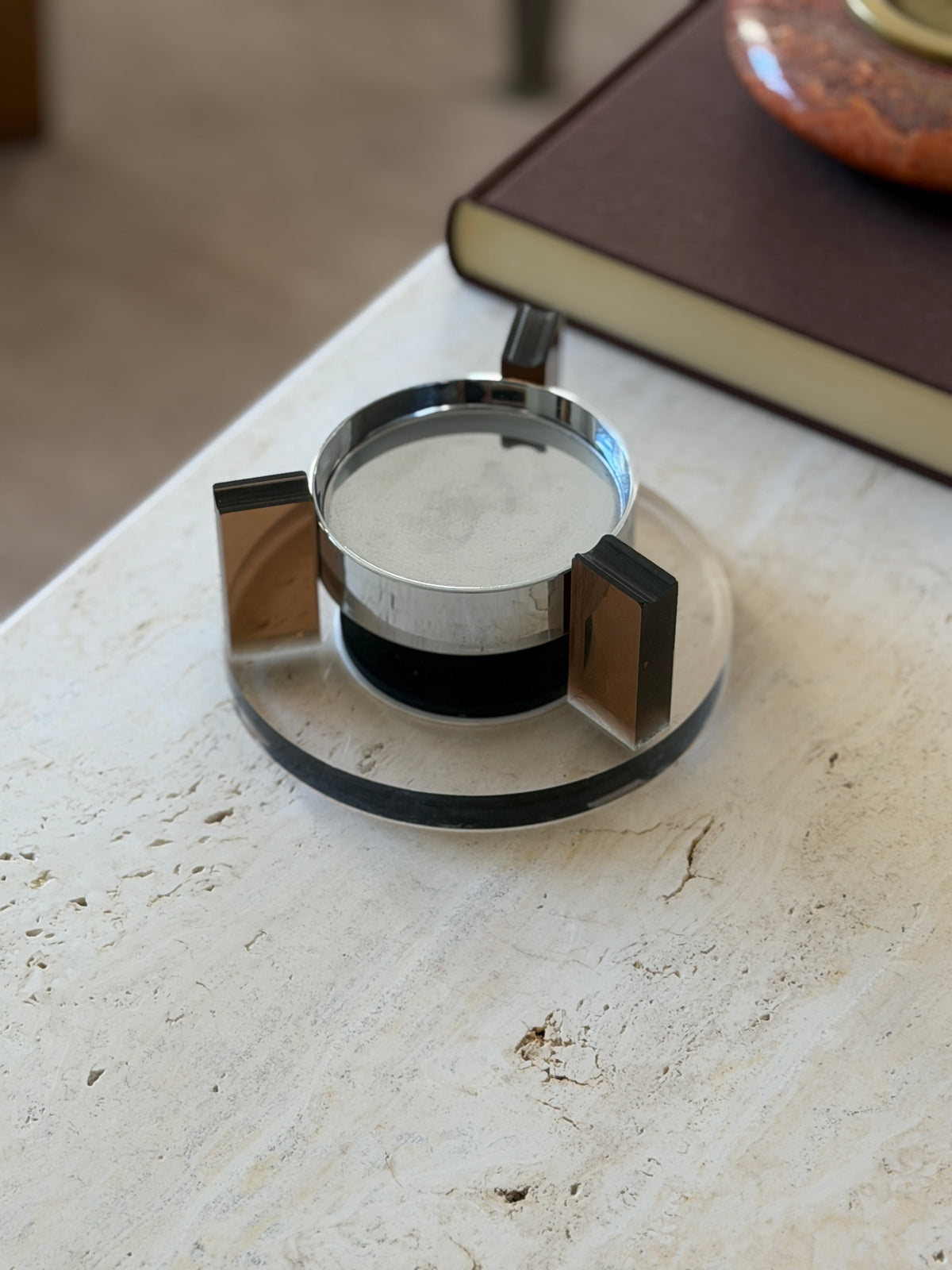 Amber Lucite and chrome magnetic floating ashtray on a round clear Lucite base, three amber uprights framing the polished chrome bowl on a travertine table