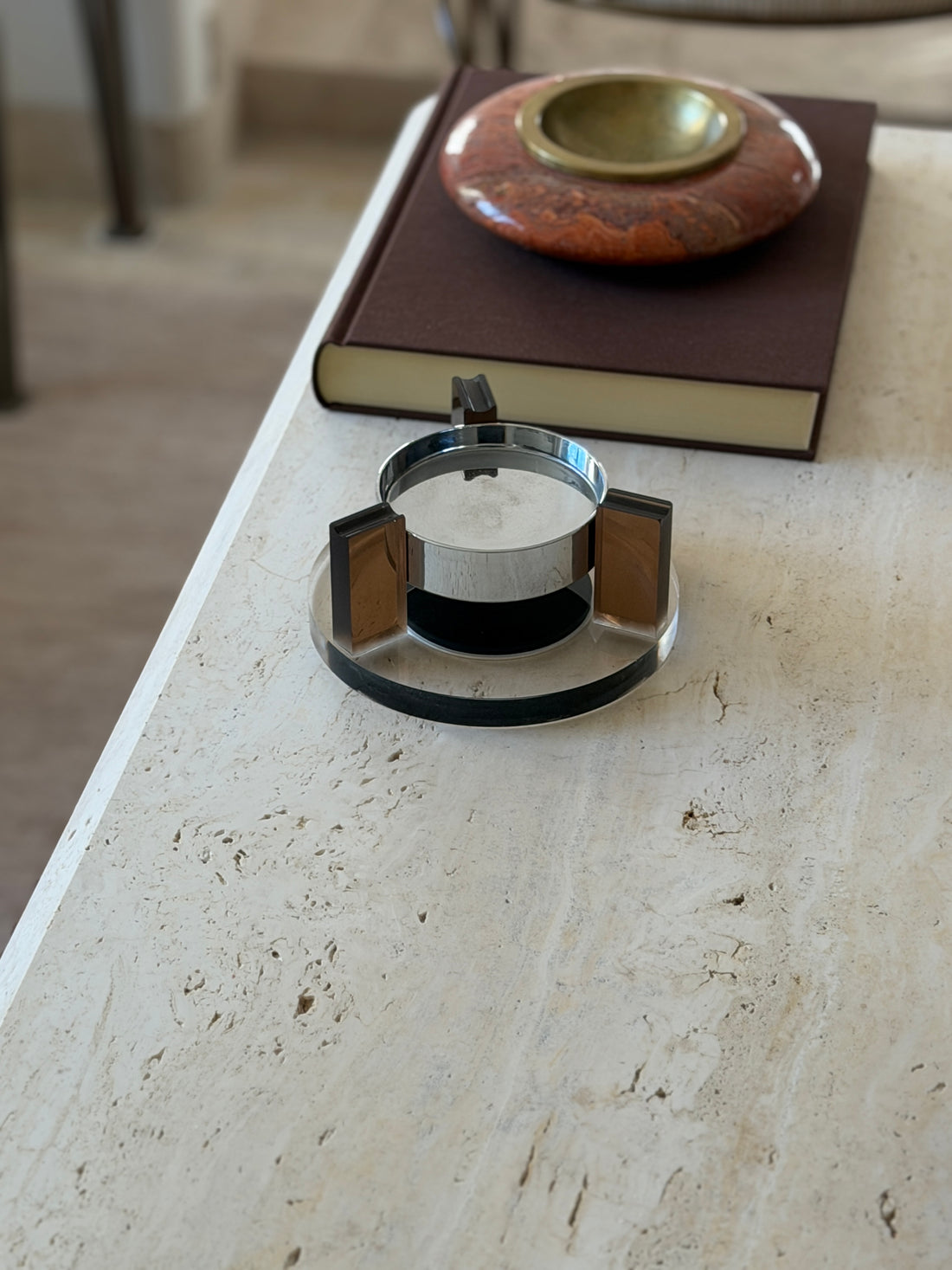 Front view of the 1970s floating ashtray with its chrome bowl suspended above a black magnetic base, a red stone ashtray on a brown book behind