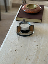 Front view of the 1970s floating ashtray with its chrome bowl suspended above a black magnetic base, a red stone ashtray on a brown book behind