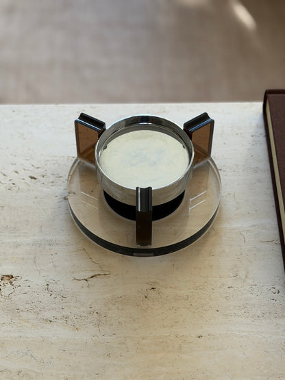 Head-on view of the round base floating ashtray showing the chrome bowl interior and three amber Lucite supports rising from the clear disc base