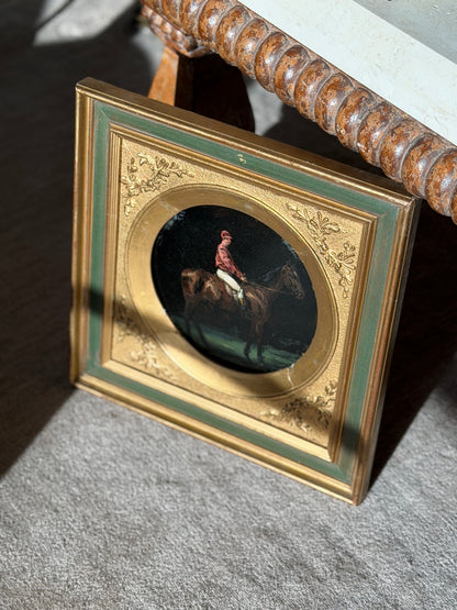 Jockey on horseback painting propped beneath a carved bobbin edge console, sunlight raking across the gilt and sage green frame