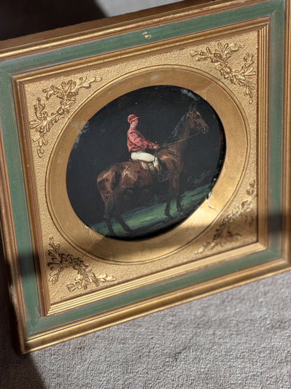 Close angled detail of the painted bay horse and red jacketed rider, with visible age cracks and losses to the gilt round mat