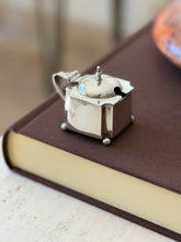 Reverse view of the silver mustard pot showing the spoon notch in the shaped lid, the scroll handle, and the shaped corner panels