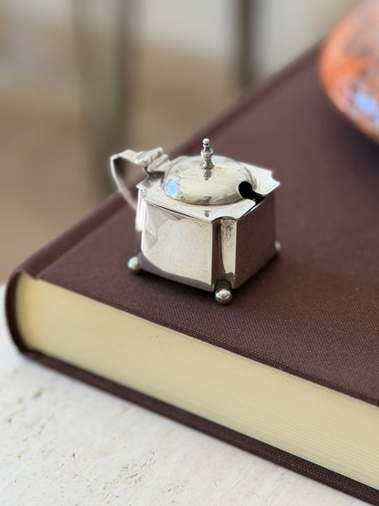 Reverse view of the silver mustard pot showing the spoon notch in the shaped lid, the scroll handle, and the shaped corner panels