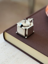 Angled view of the mustard pot on a book, the spoon slot and finial in front and a full set of hallmarks on the side panel