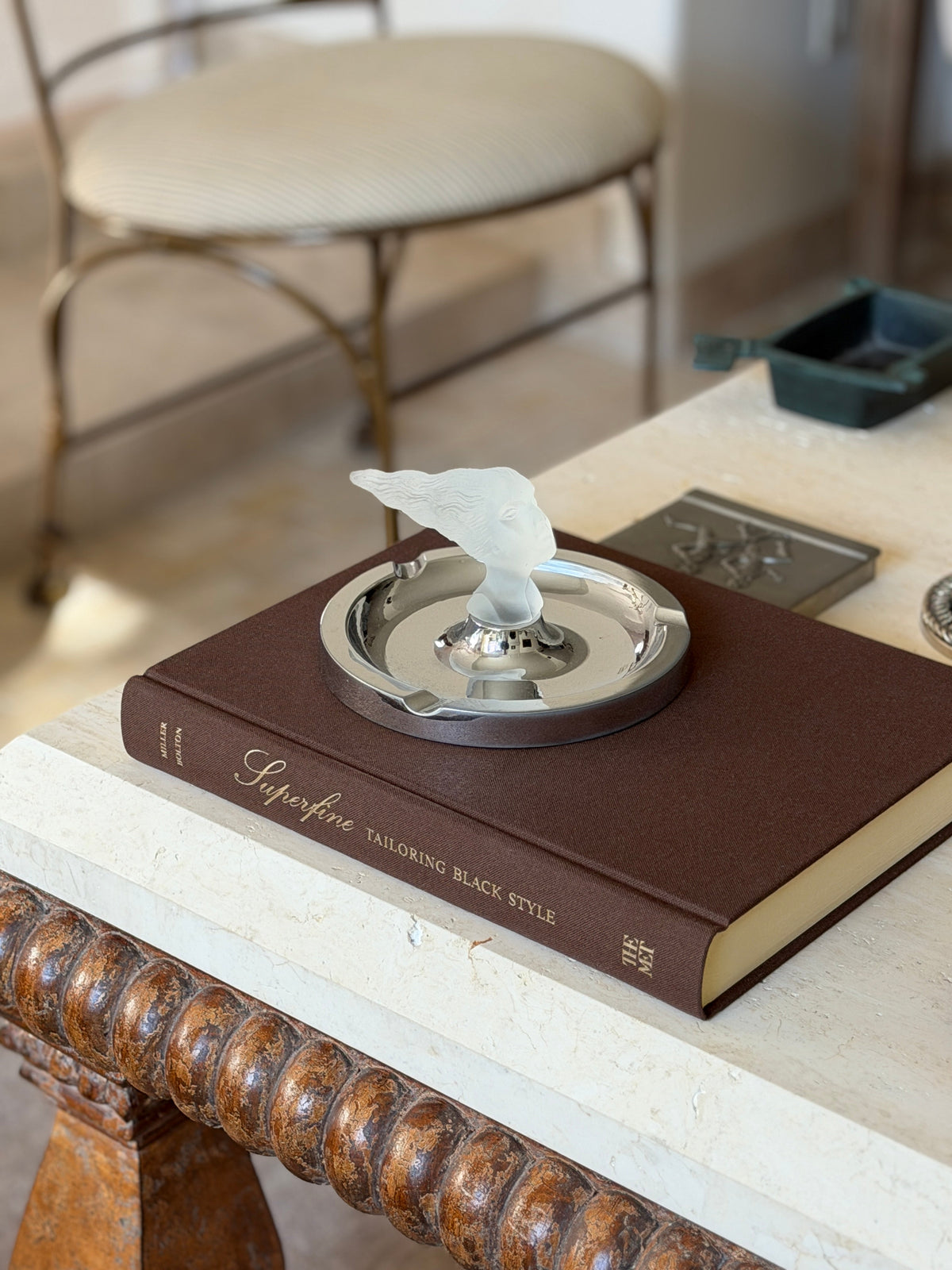 Angled view of the ashtray displayed on a book near a stool and pewter box