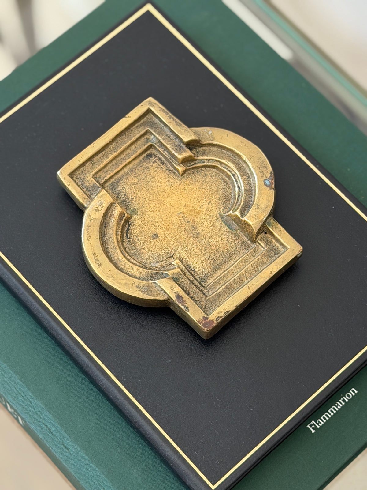 Top-down view of heavy bronze geometric vide poche showing stepped recessed borders on green display book