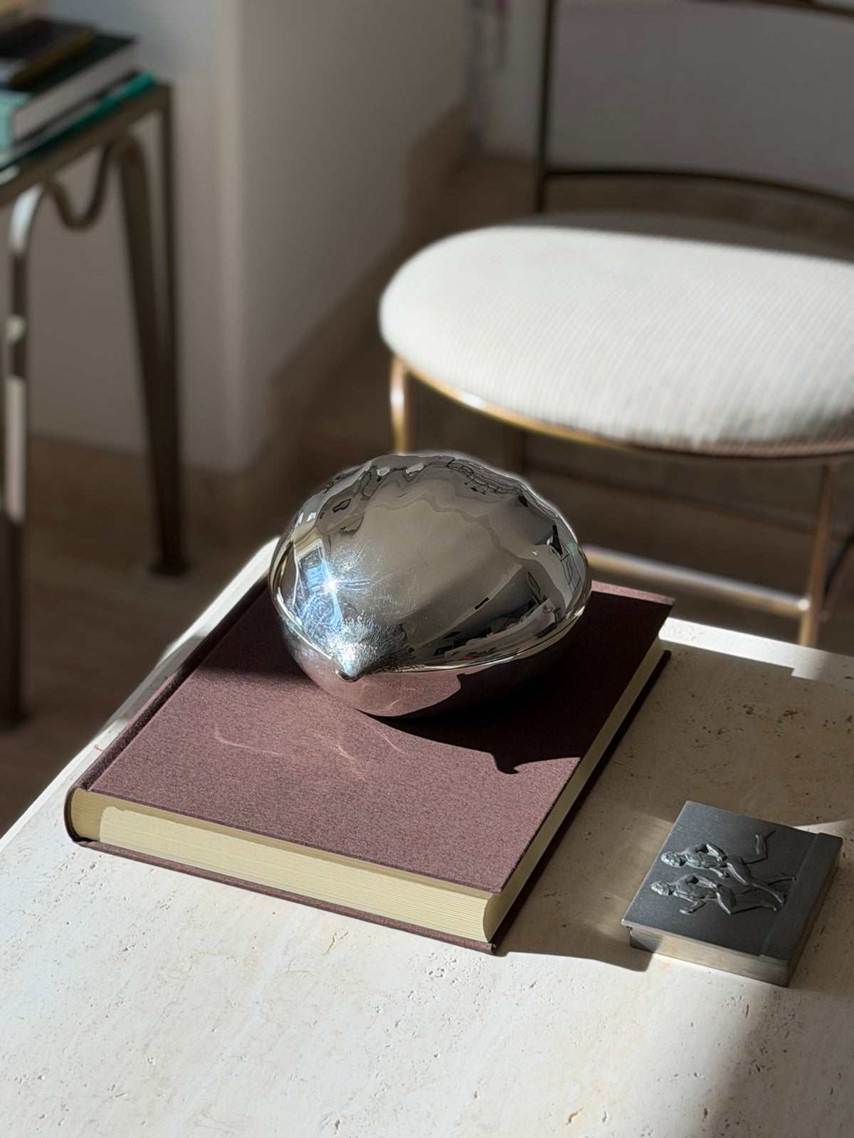 Cartier sterling silver chestnut box with a mirror polished shell and textured tip, resting on a brown clothbound book beside a pewter box with runners in relief