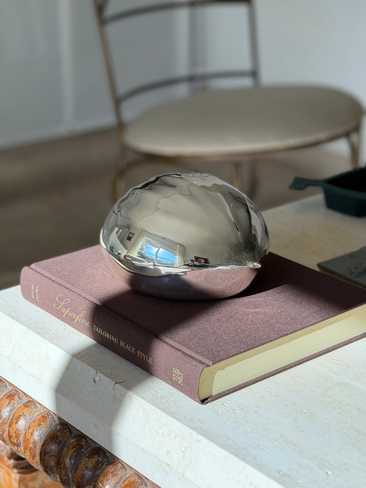 Cartier chestnut box on the Superfine Tailoring Black Style book atop a travertine console, a chair softly blurred behind