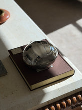 Overhead view of the Cartier sterling chestnut box on a brown book in raking sunlight, the textured shell tip at one side