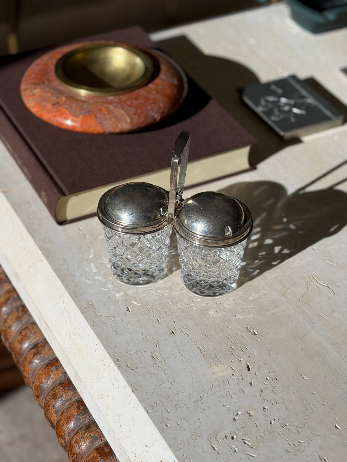 Overhead view of the Cartier jam pot, the crystal throwing diamond patterned light across the travertine beside a red stone ashtray
