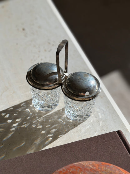 High angle view of the Cartier double jam pot on the edge of a travertine table, crystal shadows falling across the stone