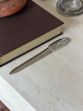 The full letter opener resting on the stone surface near the book, with a crystal coaster nearby