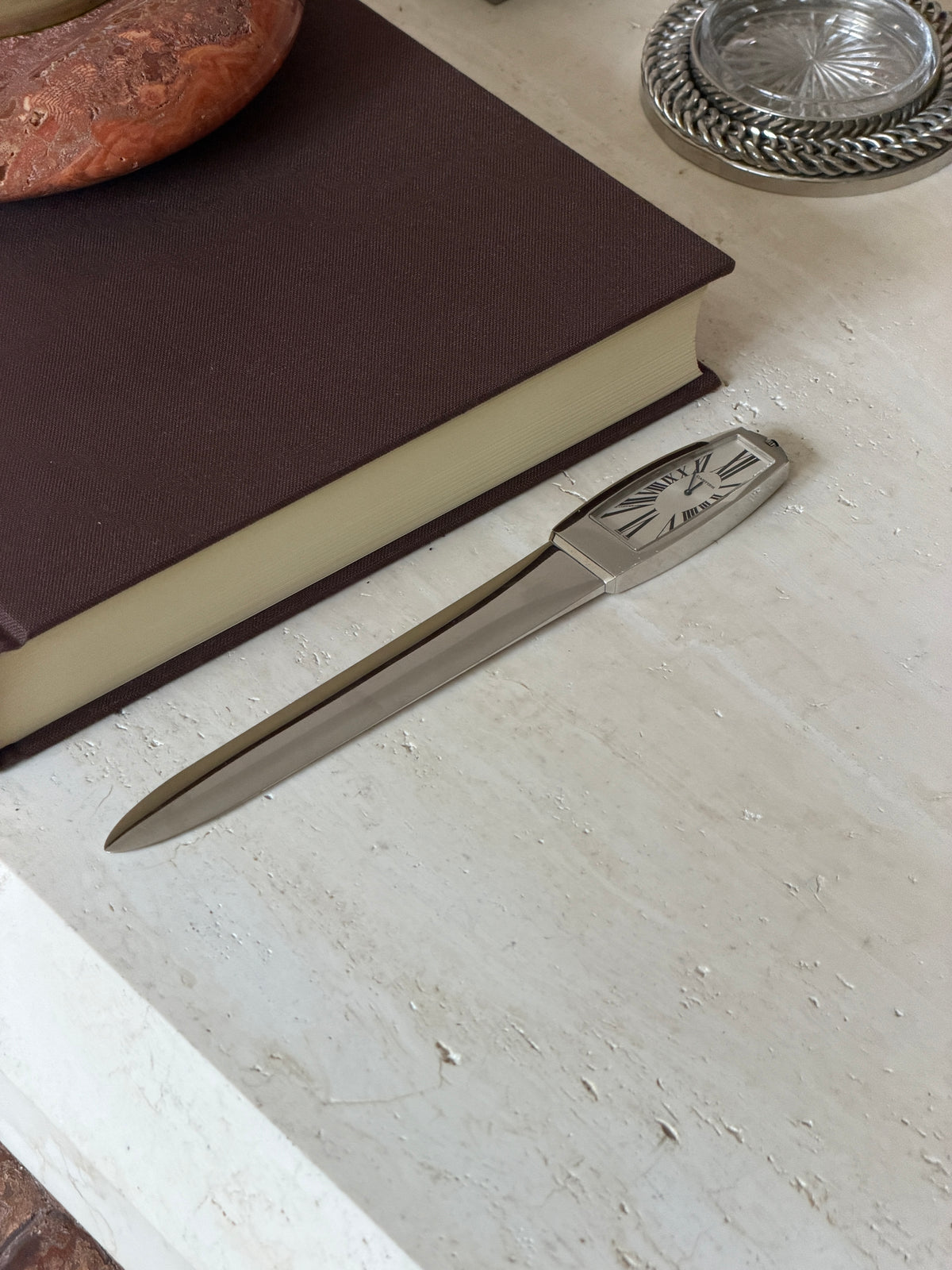 The full letter opener resting on the stone surface near the book, with a crystal coaster nearby