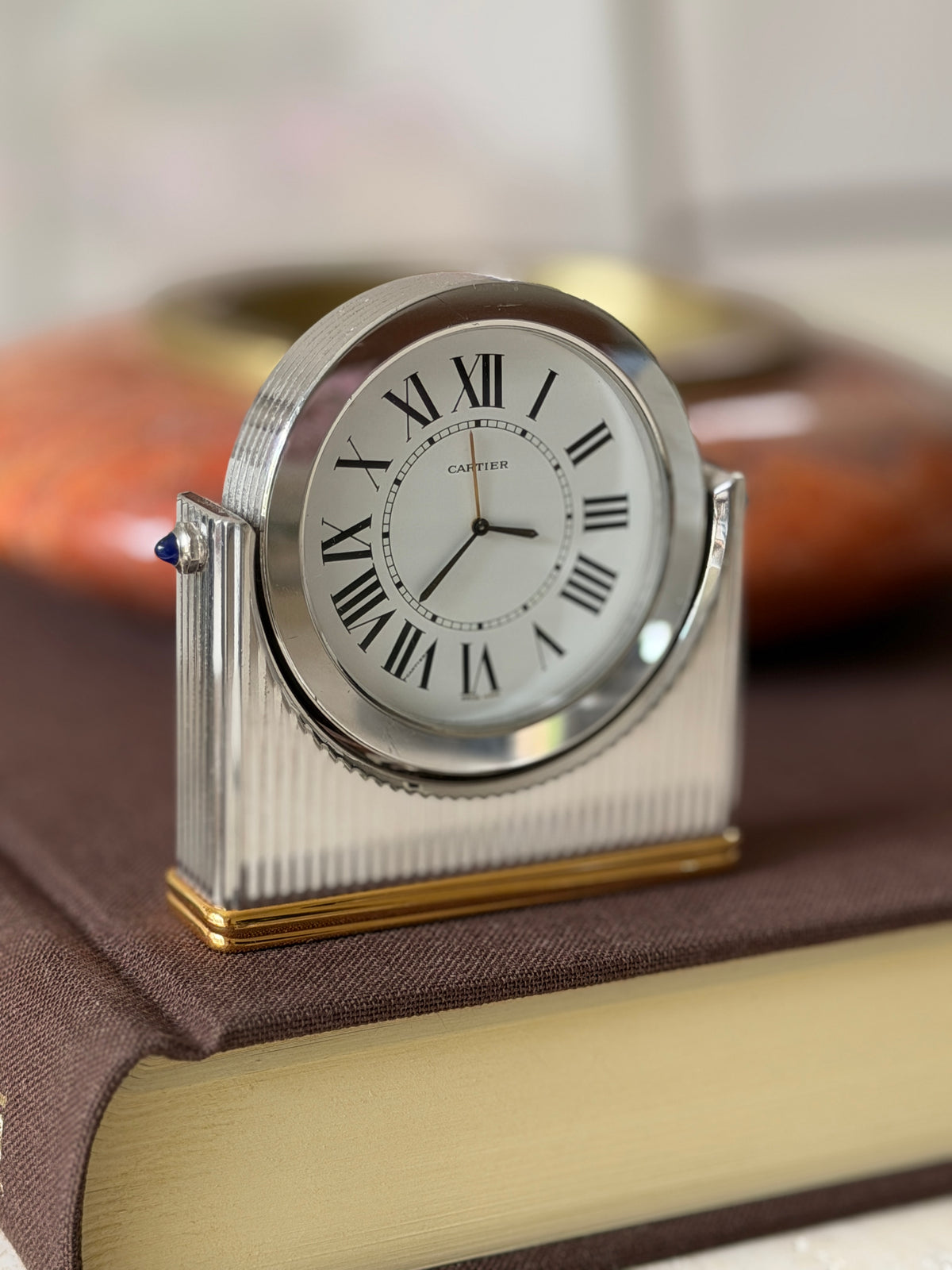 Angled close view of the Cartier Ronde desk clock with white dial, black Roman numerals, fluted silver-tone case, and sapphire cabochon