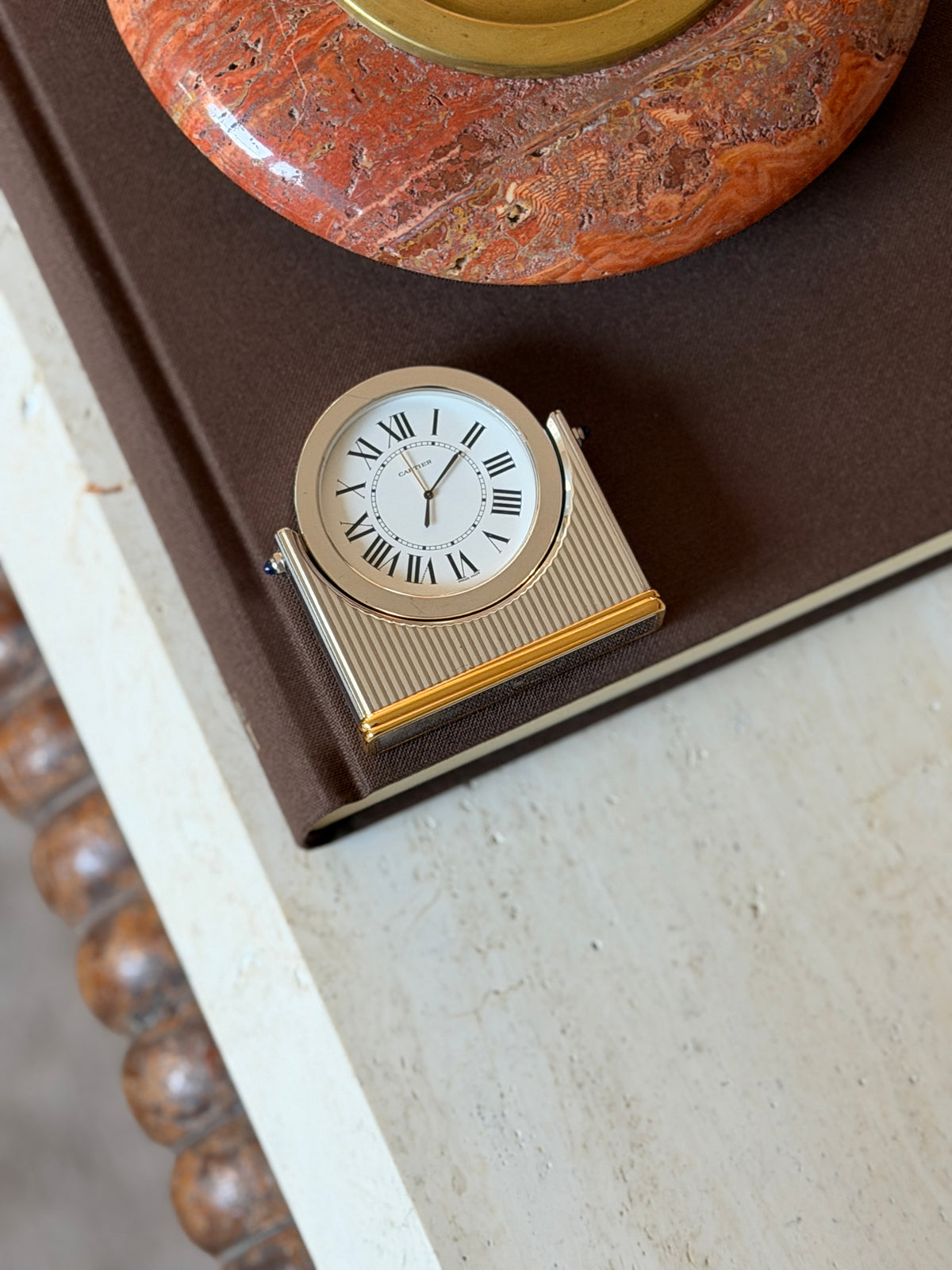 Overhead view of the Cartier desk clock on the corner of a book, showing the vertically fluted body and gold-tone banded base