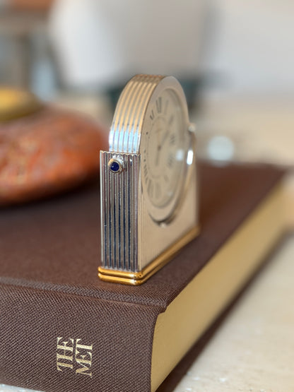 Side profile of the Cartier clock highlighting the ribbed edge of the round dial housing, a blue sapphire cabochon, and the gold-tone base