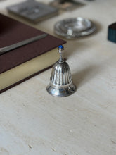 The bell viewed with a letter opener resting on the book edge and a woven silver coaster blurred behind