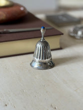 The bell shown near an orange stone bowl, a brown book, and a gray box in the background